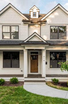 a white two story house with black roofing and large front door, on a sunny day