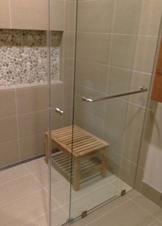 a bathroom with a glass shower door and wooden bench in the corner next to it