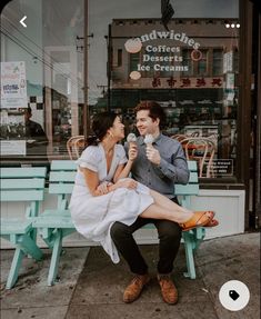 a man and woman sitting on a blue bench in front of a coffee shop eating ice cream