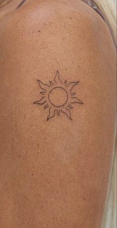 the back of a man's shoulder with a small sun tattoo on his left arm