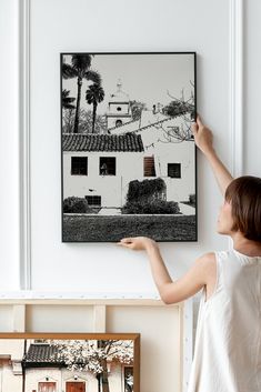 a woman is pointing at a black and white photo on the wall above her head