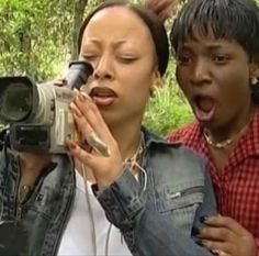 two people standing in the woods taking pictures with a camera and another person holding a video camera up to their face