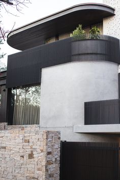 a modern house with black and white balconies on the front door, surrounded by stone walls