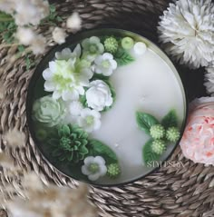 a candle with flowers on it sitting in a wicker basket next to other flowers