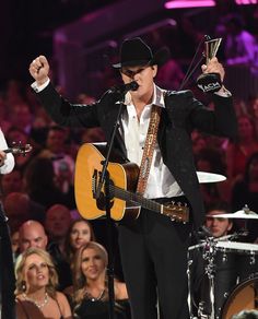 a man in a suit and hat singing into a microphone while holding an award on stage