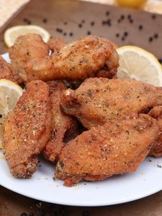 chicken wings with lemon wedges on a plate next to some black pepper flakes