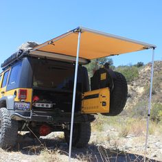 an off road vehicle is parked in the desert under a tent with its door open