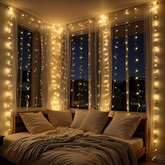 an unmade bed with lights on the windows