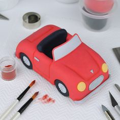 a red toy car sitting on top of a table next to some paint and brushes