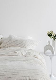 a bed with white sheets and pillows next to a vase with flowers on the side