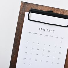 a calendar on a wooden table with a pen and paper attached to the clipboard