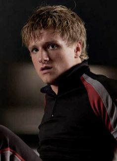 a young man with blonde hair wearing a black and red polo shirt looking at the camera