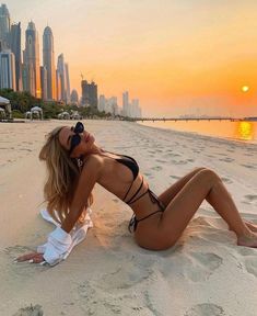 a beautiful woman laying on top of a sandy beach next to the ocean at sunset