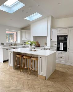 a large kitchen with an island and two stools next to it, in front of a skylight