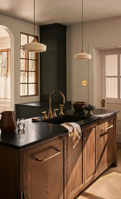 a large kitchen with wooden cabinets and black counter tops, along with two hanging lights above the sink