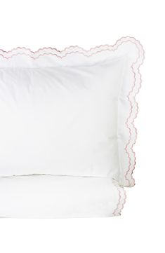 a white pillow with scalloped edges and pink piping on the side, sitting next to two pillows