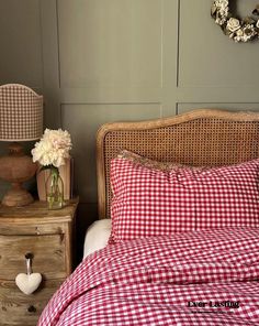 a red and white checkered comforter on a bed next to a nightstand with flowers