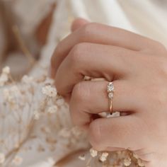 a close up of a person wearing a ring on their finger with flowers in the background