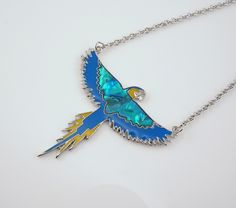 Gorgeous in both form and flight this Blue and Gold Macaw Parrot necklace is certain to delight. Made of silver tone metal with enamel and inlaid shell that's reminiscent of cloisonné, you'll find the shell colors to be richly hued and glowing every time the light hits them. The pendant measures 1 7/8 inches wide from wing to wing and is 1 7/8 inches high from head to tail. It is attached to a 19.5 inch chain (includes pendant) and is unmarked. The necklace is in excellent, new condition and perfect for gift-giving. While here be sure to see the matching pair of earrings for a truly fabulous flock and a similar necklace with a Greenwing Macaw. Greenwing Macaw, Flying Parrot, Parrot Jewelry, Blue And Gold Macaw, Parrot Necklace, Vintage Parrot, Macaw Parrot, Bird Jewelry, Necklace Blue