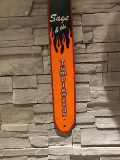 an orange and black snowboard hanging from the side of a stone wall with flames on it