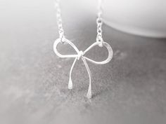 "This may be my new favorite! Sweet little handmade bow made from .925 sterling silver wire; hammered in spots for strength and design. Delicate simple chain is also .925 sterling silver oval link with a .925 sterling silver round spring clasp. **Please Note: The necklace in the photos has sold. Your bow will be the same, but not necessarily identical to the one shown, as each is handmade / hand-wrapped wire that I lovingly make one at a time. :) Bow and chain are shiny polished silver- please n Bow Pendant, Simple Chain, Silver Ribbon, Ribbon Necklace, Bow Necklace, Silver Bow, Handmade Bows, Necklace Dainty, Delicate Necklace