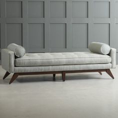 a white couch sitting on top of a wooden frame in front of a gray wall