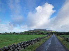 an empty road in the middle of a grassy field with a stone wall on either side