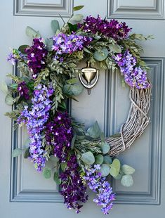 a wreath with purple flowers and greenery hanging on a door