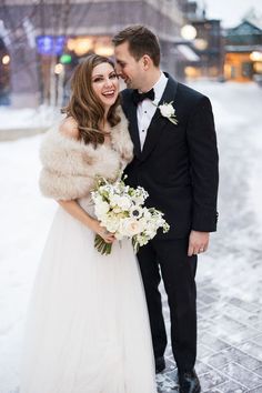 a bride and groom pose for a photo in the snow at their winter wedding ceremony