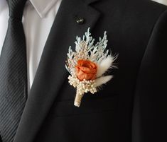 a boutonniere with an orange rose and white feathers on the lapel