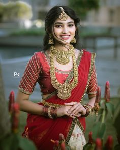 a woman in a red and white sari with gold jewelry on her neck posing for the camera