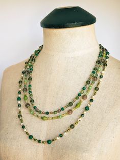 The captivating "Golden Green" necklace is a stunning combination of various beads in an array of shapes, sizes, and colors. This necklace features an eclectic mix of materials including glass, Malachite, Moss Tree Agate, Frosted Yellow Turquoise, Citrine, Purple Dyed Quartz, Diopside, Green Jade, textured and smooth golden metal, and acrylic. Each strand of this necklace is carefully crafted to showcase the unique beauty of its components adorned with a lush assortment of beads in vibrant shade Czech Glass Beaded Chain Necklace, Czech Glass Beaded Chain Necklace With Round Beads, Artisan Green Beaded Gems And Cabochons, Beaded Long Necklace Gems And Cabochons For Jewelry Making, Multi-strand Czech Glass Beaded Necklace, Long Gemstone Beads Necklace, Green Beaded Long Crystal Necklace, Green Oval Beaded Chain Jewelry, Multi-strand Necklaces With Spacer Beads For Jewelry Making