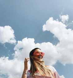 a woman wearing red sunglasses standing under a cloudy blue sky