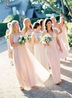 a group of women in long dresses walking down a road together with bouquets on their heads