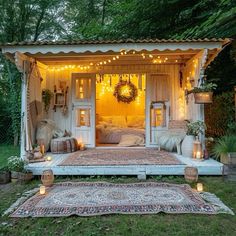 a small white shed with lights on the roof and bed in the doorway, surrounded by greenery