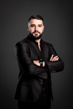 a man with his arms crossed standing in front of a black background