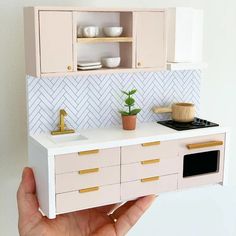 a hand holding up a dollhouse kitchen with white cabinets and gold trimmings