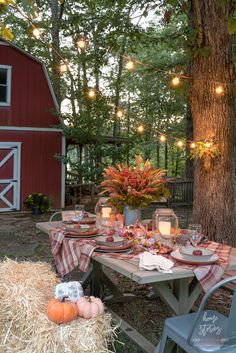 an outdoor table set up for dinner with hay and pumpkins