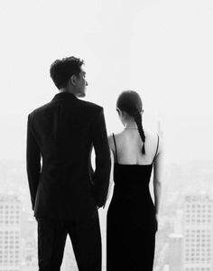 a man and woman standing in front of a window looking out at the city skyline