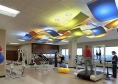 people in a gym with exercise equipment and colorful lights hanging from the ceiling above them