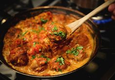 meatballs in tomato sauce with parsley being stirred by a wooden spoon on the stove