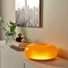 an orange light sitting on top of a white shelf next to a plant and books