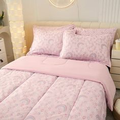 a bed with pink comforter and pillows in a white room next to a night stand