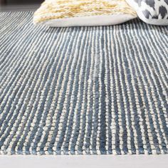 a blue rug with yellow and white pillows on it in front of a bed frame