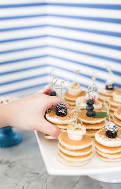 a person holding a plate with pancakes and berries on top of it, while another hand reaches for the pancakes