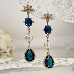 Dive into the elegance of the past with our Navy Blue Art Deco Earrings, a perfect blend of Art Nouveau charm and Bohemian chic. Each earring begins with a beautifully detailed floral post, encrusted with clear zirconia crystals, leading to a mesmerizing navy oval crystal, surrounded by four petite zirconias. Below, a delicate white crystal pearl adds a touch of romantic Coquette flair, trendy for both everyday fashion and chic boho weddings. The pièce de résistance is the navy blue crystal tear Romantic Coquette, Art Nouveau Earrings, Earrings For Bride, Navy Blue Art, Unique Graduation Gifts, Earrings Boho Chic, Art Nouveau Earring, Marine Art, Pearls Earrings