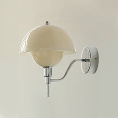 a wall light with a white glass shade on it's arm and the bulb turned off