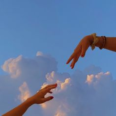 two hands reaching out towards each other in the sky with white clouds behind them,