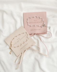 two personalized wedding gifts are laying on a white bed with the bridesmaid tag attached to it