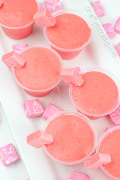 three cups filled with pink candy sitting on top of a white table next to cubes